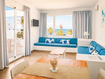 Helles Wohnzimmer mit blauen Sitzpolstern, weißen Möbeln, großen Fenstern und Zugang zur Terrasse.