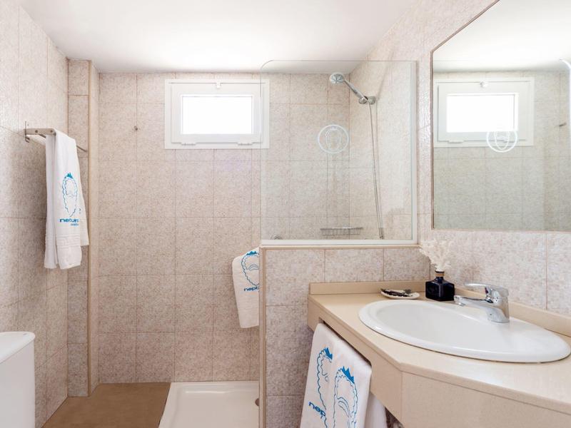 Bright bathroom with shower, sink, mirror, and towels in neutral tones.