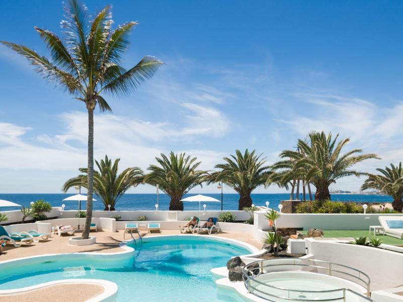 Pool area with palm trees and ocean view under a blue sky
