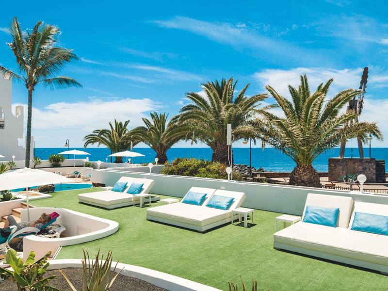 Modern lounge seating with white sofas and a view of the sea under sunny weather.