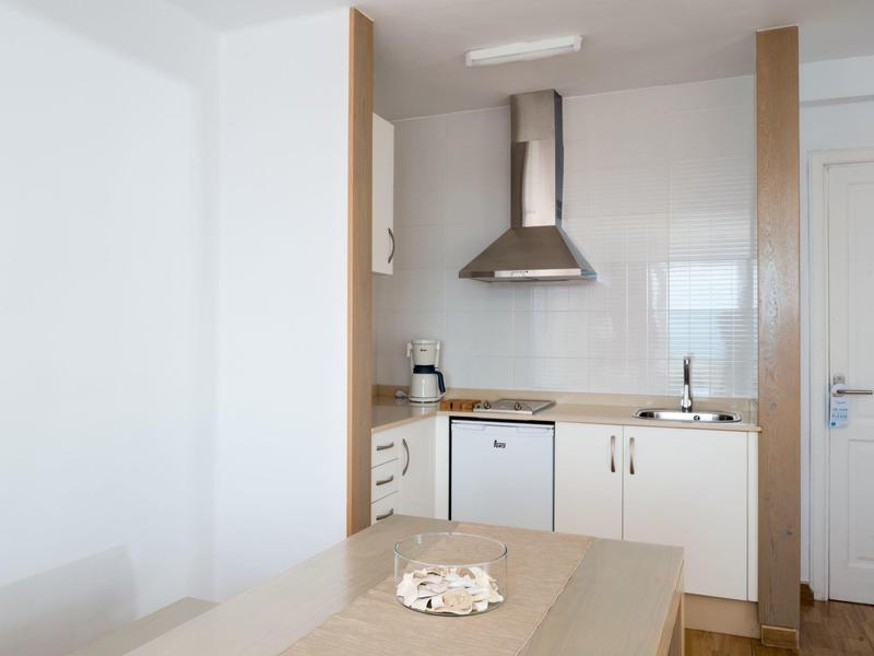 Modern small kitchenette with white cabinets, extractor hood, and small stove in a hotel room.