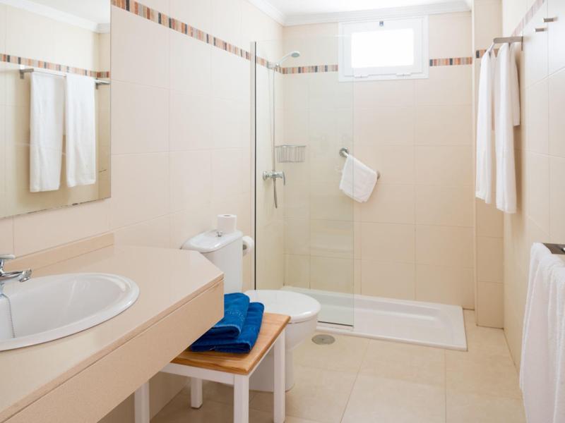 Bright bathroom with shower, sink, towels, and a small stool holding blue towels.