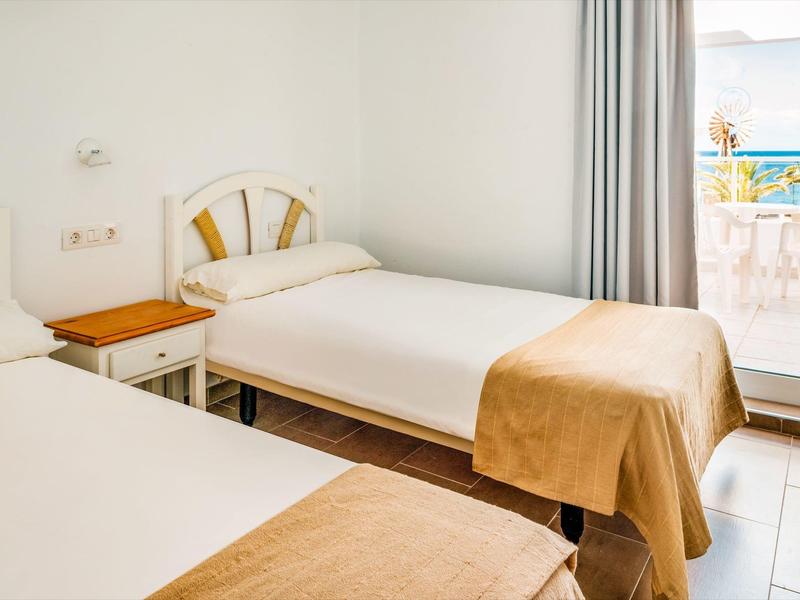 Brightly furnished hotel room with two single beds and balcony with sea view.