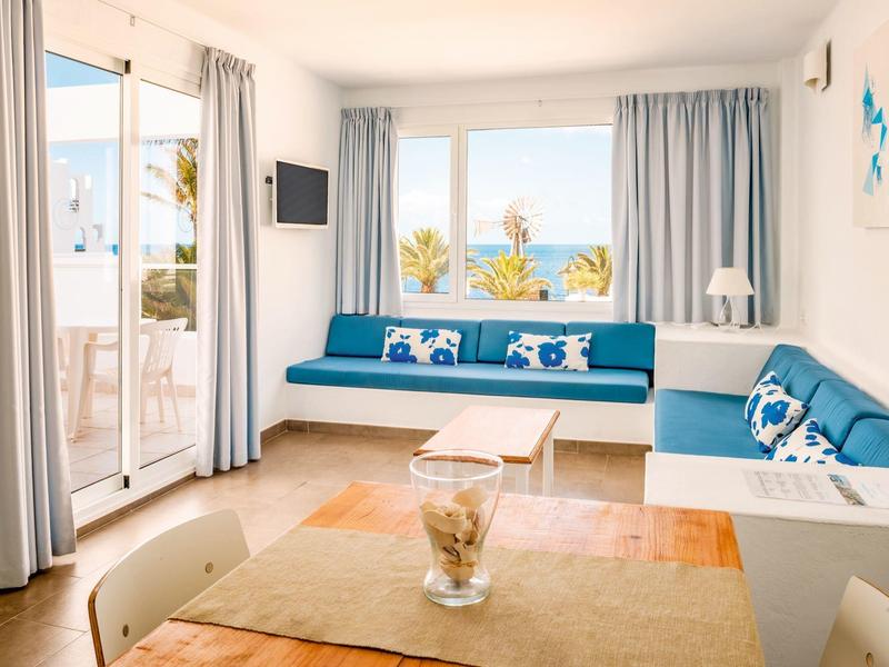 Bright living room with blue sofas, large window, and terrace overlooking the sea.