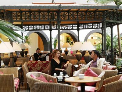 Cozy hotel outdoor patio with rattan furniture and plants, guests relaxing and chatting.