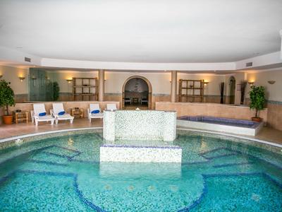 Indoor pool with round basin and seating area in a bright spa setting.