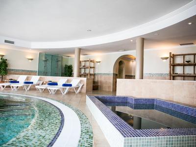 Vnitřní bazén s lehátky a malým vířivým bazénem v moderním lázeňském zařízení.