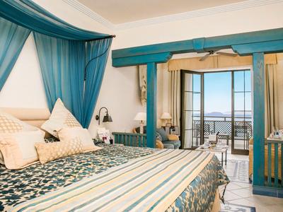 Elegant bedroom with large bed, blue curtains, and view of terrace and sea.