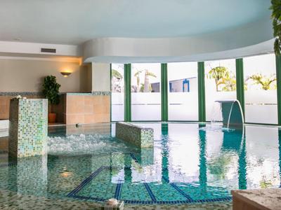 Vnitřní bazén s velkými okny, rostlinami a dlažbou obklopenou kamennou podlahou.