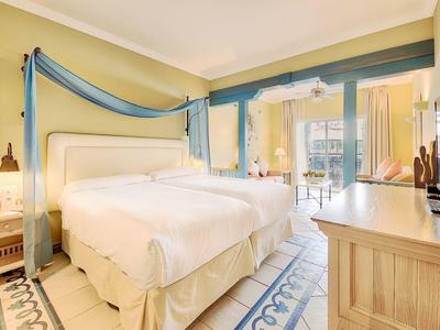 Světý hotelový pokoj s velkou postelí, dřevěným nábytkem a balkonem s výhledem na město.