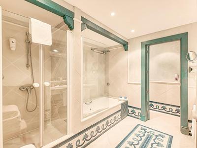 Světlá koupelna se sprchou, vanou, velkým zrcadlem a dekorativními obkladovými dlaždicemi.