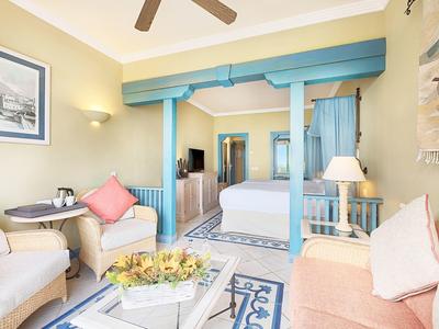 Světelný hotelový pokoj s pastelovým nábytkem, postelí a útulným posezením s polštáři.