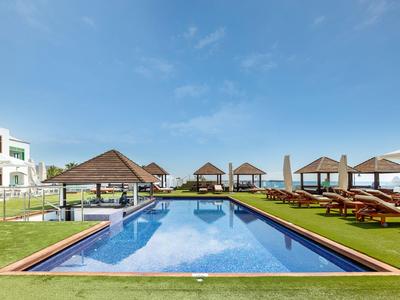 Modern pool with sun loungers and umbrellas under clear sky at a hotel resort.