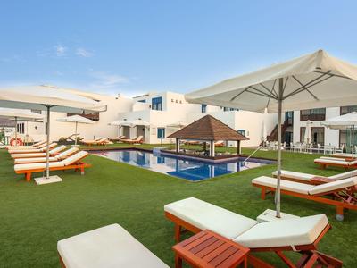 Modern outdoor area with pool, sun loungers, umbrellas, and white building in the background.
