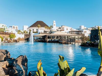 Rezort s bílými budovami kolem velké modré laguny a fontánou pod jasnou oblohou.