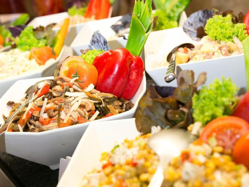 Barevné saláty z zeleniny a obilovin podávané v bílých miskách na bufetovém stole.