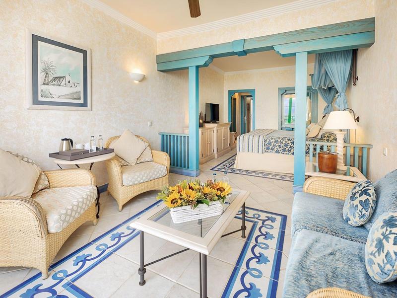 Pohodlný sedací kout s béžovými křesly, modrou pohovkou a dekorativními květinami v místnosti s plážovým motivem.