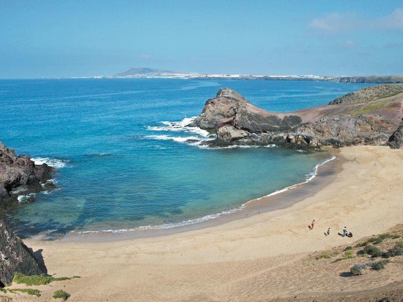 Osamělá písečná pláž s kamennými útesy a klidným modrým mořem pod jasnou oblohou.