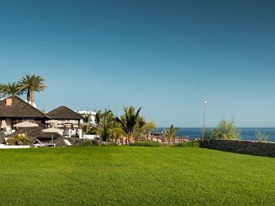 Prato verde davanti a un hotel sul mare sotto un cielo azzurro limpido.