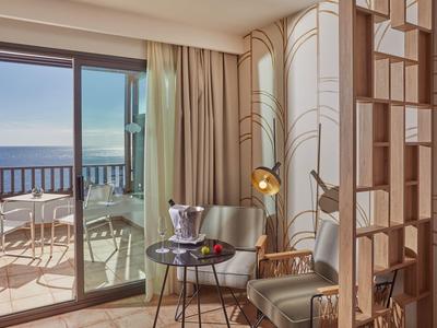 Camera d'hotel con vista mare, due poltrone, tavolino e balcone con posti a sedere.