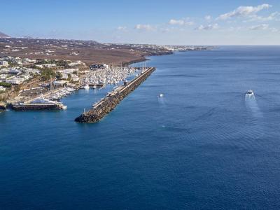 Veduta aerea di un molo del porto con città costiera circostante e mare blu profondo sotto un cielo limpido.