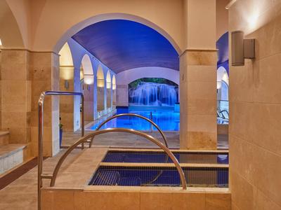 Area piscina interna con vasche idromassaggio riscaldate e grande piscina sotto una volta blu.