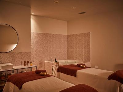 Accogliente stanza benessere con lettini da massaggio, luce calda e specchio rotondo a parete.