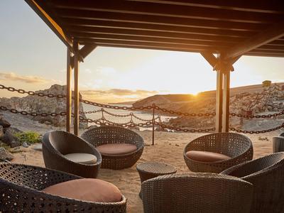Accogliente lounge esterna con sedie in vimini rotonde che si affacciano su una spiaggia soleggiata al tramonto.
