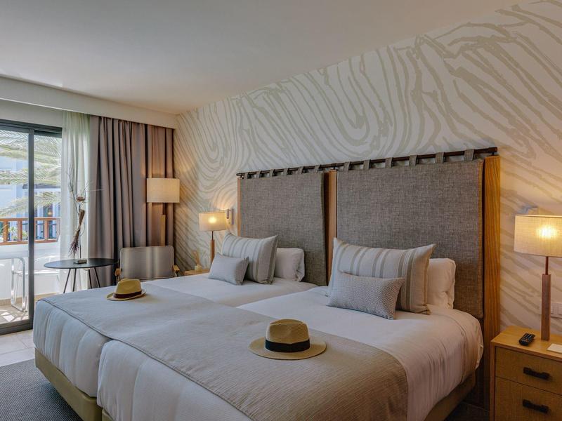 Camera d'hotel moderna con due letti, lampade e balcone con vista sulle montagne.