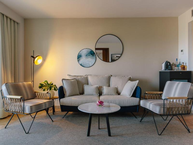 Zona giorno moderna con poltrone chiare, divano, specchi rotondi e tavolino.