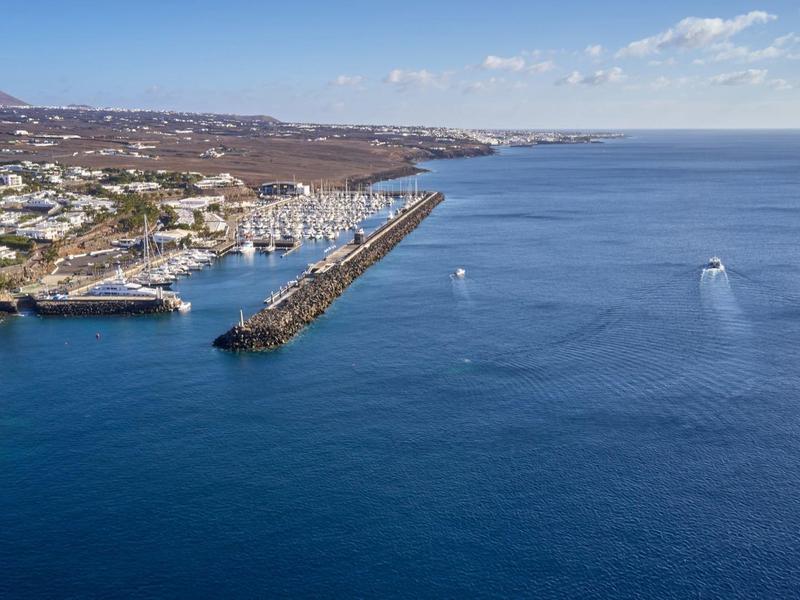 Veduta aerea di un molo del porto con città costiera circostante e mare blu profondo sotto un cielo limpido.