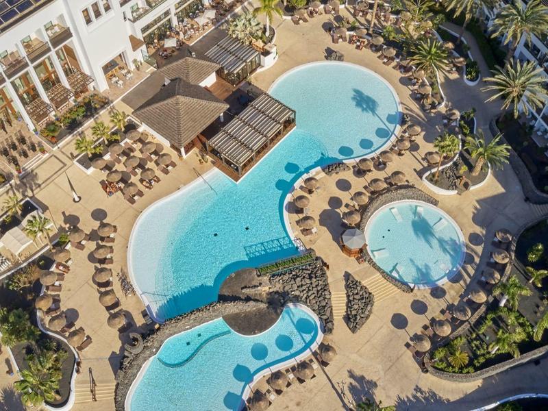 Vista aerea di una piscina d'hotel con ombrelloni e sdraio.