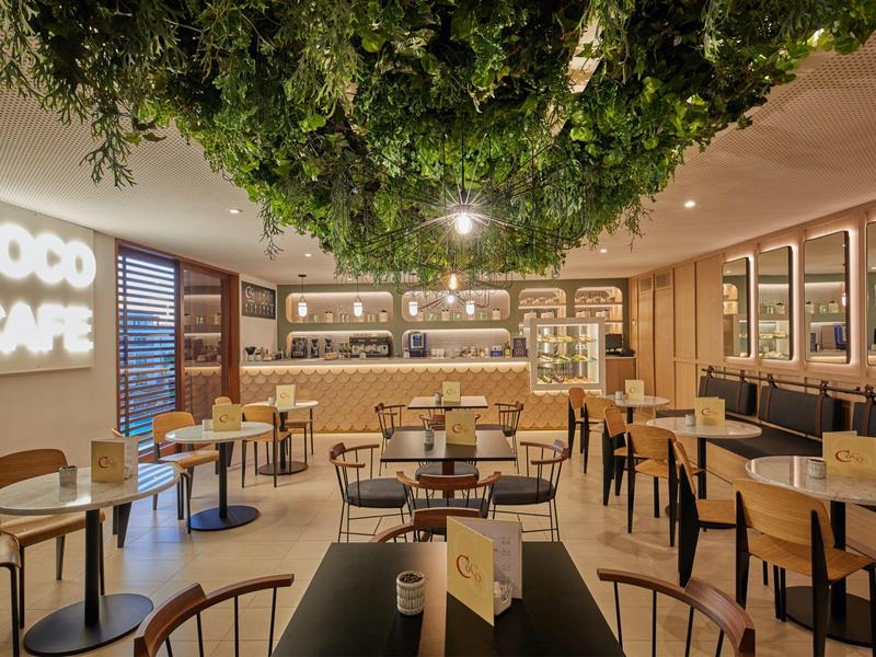 Area caffè moderna con mobili in legno, insegna Coco Cafe illuminata e atmosfera accogliente.