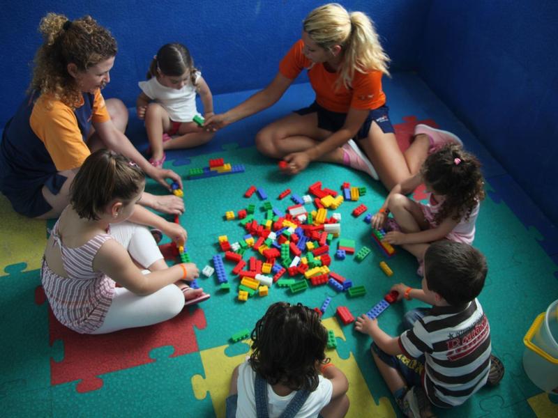 Kinderen zitten in een cirkel en spelen met kleurrijke bouwblokken op een mat.