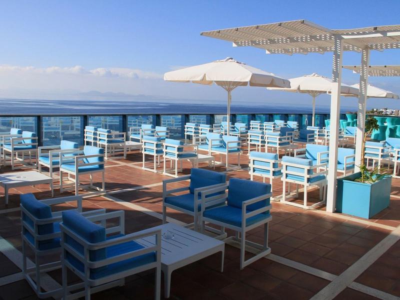 Buitenterras met blauw gevoerde stoelen en tafels met uitzicht op zee onder parasols.