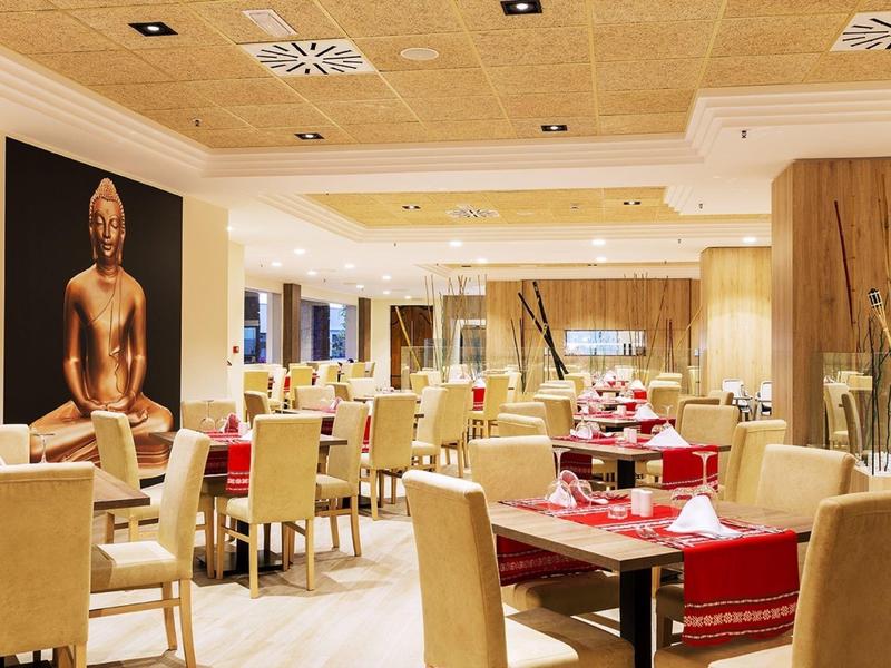 Licht hotelrestaurant met beige stoelen, rode tafellopers en een Boeddha wanddecoratie.