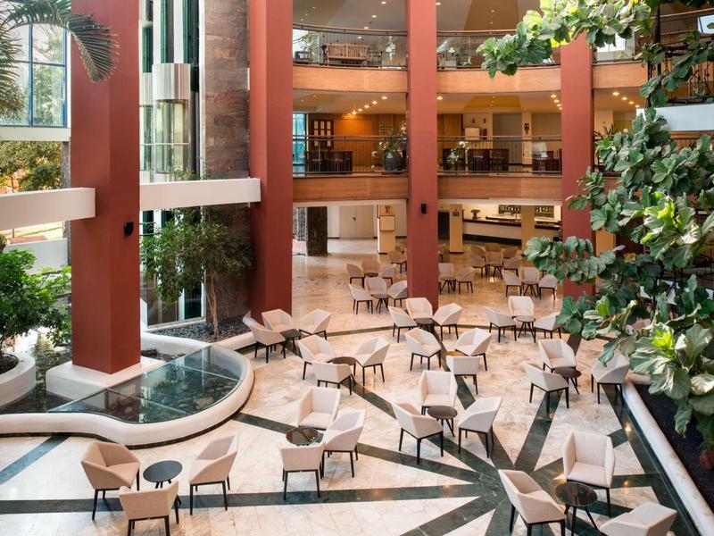 Ruime hotellobby met zitgedeelte, binnenplanten en een waterornament.