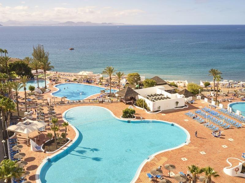 Groot hotelzwembad met uitzicht op de oceaan, ligstoelen en parasols op een zonnige dag.