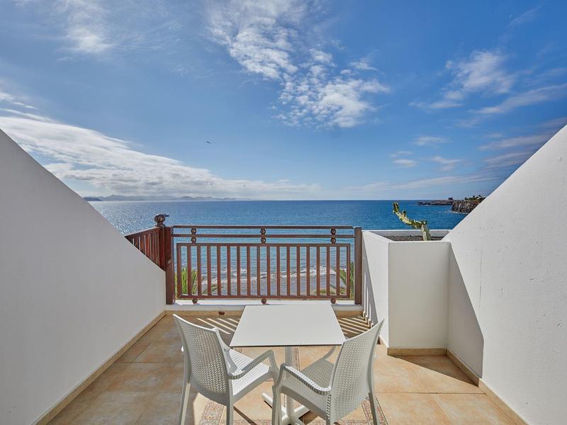 Balkon met tafel, stoelen en uitzicht op de oceaan onder een deels bewolkte lucht.