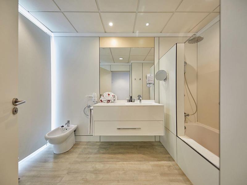 Moderne badkamer met grote spiegel, witte wastafel, bidet en bad met glazen scherm.