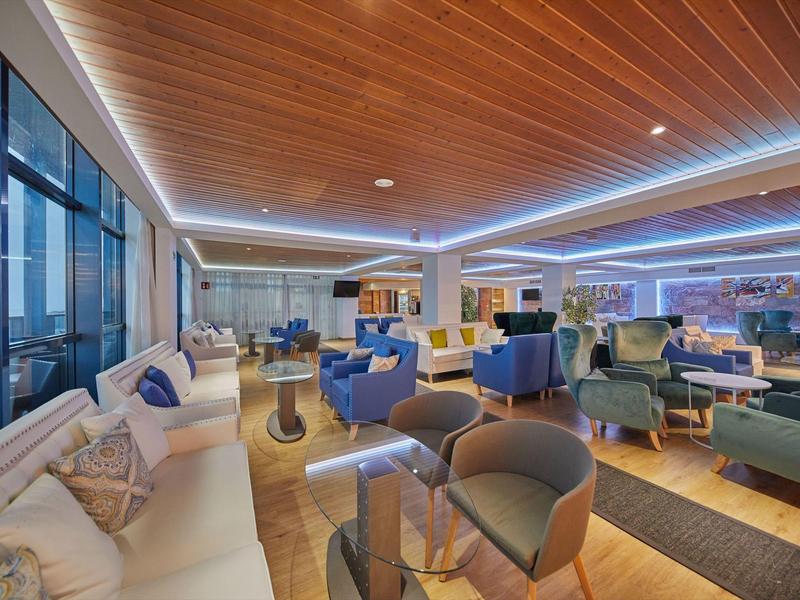 Ruime moderne hotel-lounge met houten plafond, zachte verlichting en diverse zitopties.