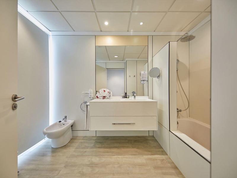 Moderne badkamer met ligbad, zwevende wastafel, bidet en grote spiegel onder inbouwspots.