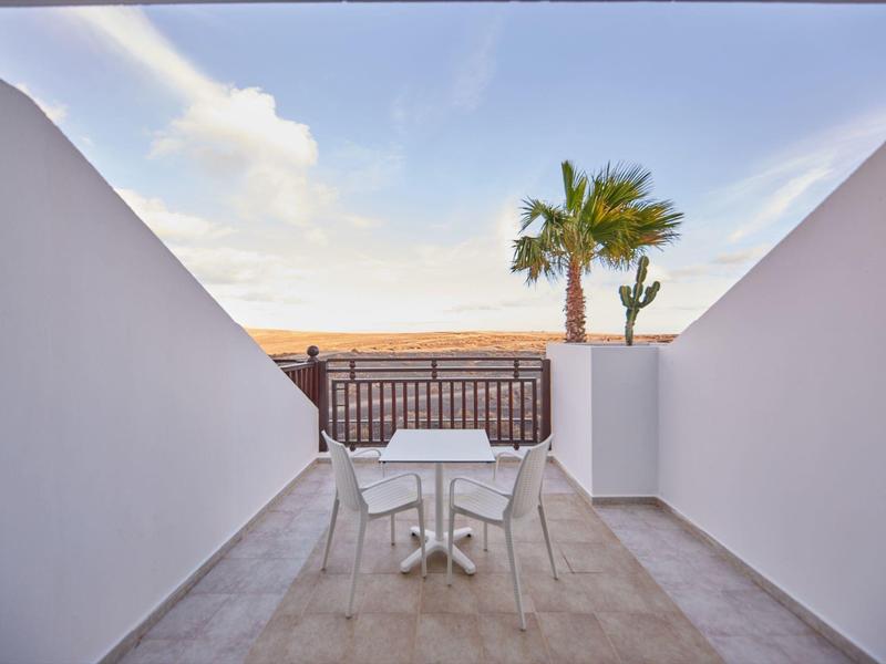 Buitenterras met witte tafel en stoelen met uitzicht op een palmboom en oceaanhorizon.