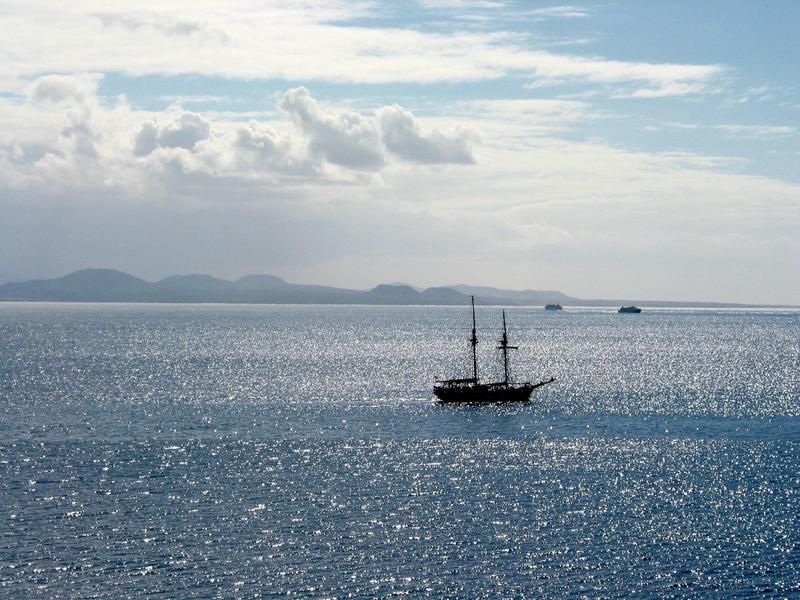 Lichte hotelkamer met bed, grijze bank, glazen tafel en keukenhoek.