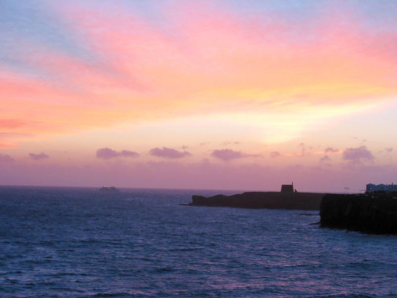 Prachtig uitzicht op de oceaan bij zonsondergang met roze en oranje lucht boven rotsen en rustige zee.