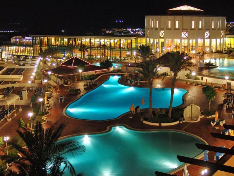 Nachtzicht op een luxe hotelresort met verlichte zwembad en ligstoelen