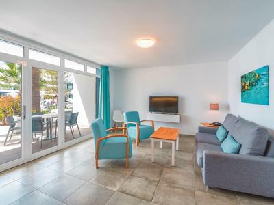 Heller Wohnraum mit großen Fenstern, grauem Sofa, türkisen Stühlen und Holztisch.