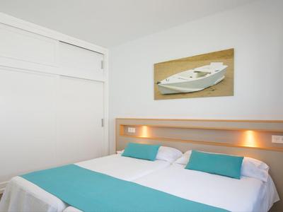 Helles Schlafzimmer mit Doppelbett, weißen Wänden, türkisfarbenem Bettläufer und Bootbild an der Wand.