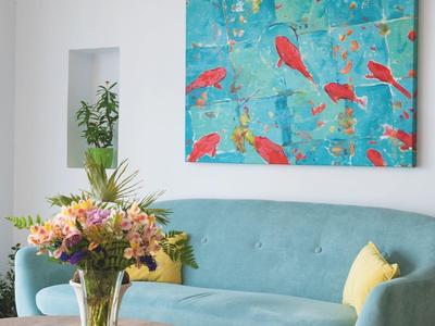 Wohnzimmer mit blauem Sofa, rundem Holztisch, Blumenstrauß und bunter Wandkunst.