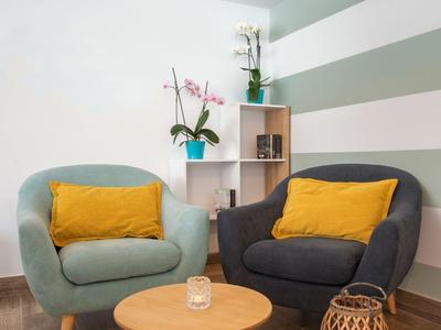 Kleiner Wohnbereich mit zwei Sesseln, gelben Kissen, rundem Holztisch und gestreifter Wand.